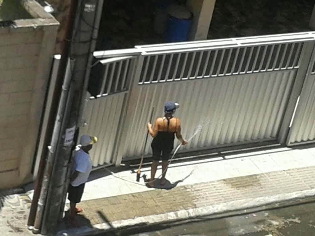 Moradora usando água para “lavar” o portão. Foto Divulgação.