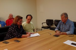 Núbia Lorenzutti, diretora da empresa vencedora do edital, assina o contrato observada pelo pai, Claudinor, fundador a Asatur. Foto: João Thomazelli/Portal 27